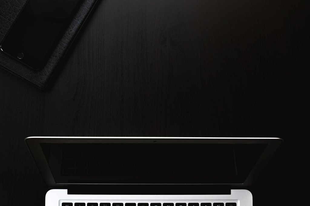 A sleek and minimalist workspace featuring a laptop and smartphone on a dark surface.